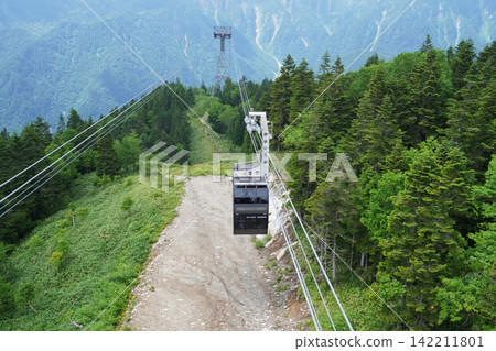 The scenery of the cable car traveling up the slopes through the beautiful alpine forest. The scenery of the cable car traveling up the slopes through the beautiful alpine forest. 142211801