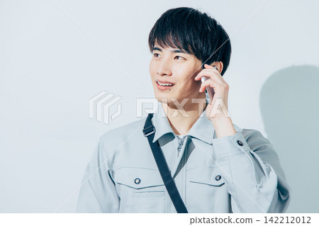 Man in work clothes operating a smartphone Man in work clothes operating a smartphone 142212012