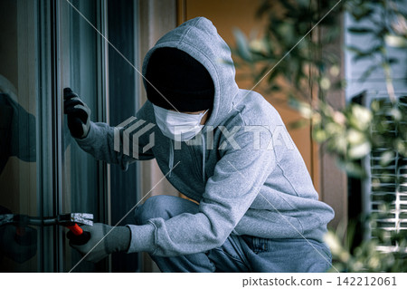 A young man, a suspicious individual, attempts to break a balcony window. A young man, a suspicious individual, attempts to break a balcony window. 142212061