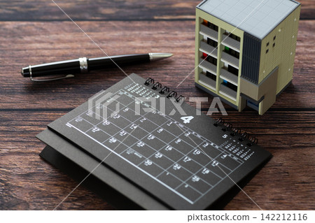 A black calendar for April and a model of an apartment building. A black calendar for April and a model of an apartment building. 142212116
