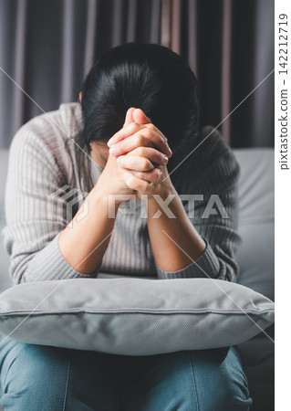 Adult woman sitting with bowed head and clasped hands, praying or reflecting during a difficult time, symbolizing faith, hope, emotional struggle, healing, and spiritual support. Adult woman sitting with bowed head and clasped hands, praying or reflecting during a difficult time, symbolizing faith, hope, emotional struggle, healing, and spiritual support. 142212719