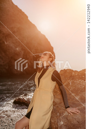 Woman beach sunset elegant woman posing against a rocky cliff at the seashore during golden hour in a stylish yellow vest Woman beach sunset elegant woman posing against a rocky cliff at the seashore during golden hour in a stylish yellow vest 142212940