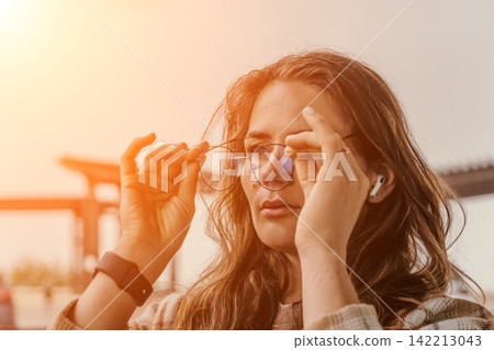 Woman eyeglasses sunset Young woman holding glasses while wearing wireless earbuds and smartwatch outdoors in golden hour Woman eyeglasses sunset Young woman holding glasses while wearing wireless earbuds and smartwatch outdoors in golden hour 142213043