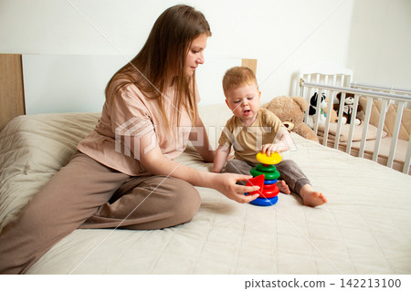 Toddler sorting colorful pyramid pieces. Logic development through play. Colorful educational toy supports natural curiosity and brain development Toddler sorting colorful pyramid pieces. Logic development through play. Colorful educational toy supports natural curiosity and brain development 142213100