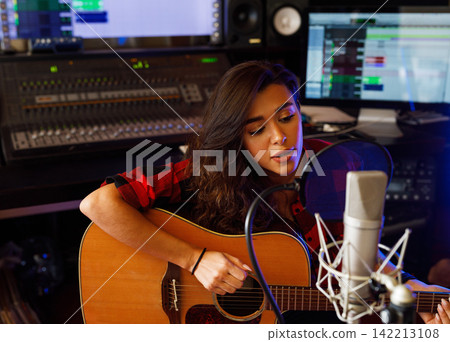 Young female singer with acoustic guitar recording a song promo in a studio Young female singer with acoustic guitar recording a song promo in a studio 142213108