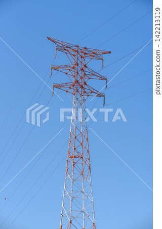 A tall red and white high-voltage electricity pylon dominating a vast clear blue sky in a low-angle shot A tall red and white high-voltage electricity pylon dominating a vast clear blue sky in a low-angle shot 142213119
