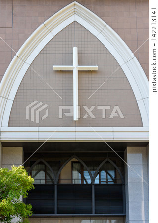 A close-up view of a modern church's facade featuring a large white cross mounted in a prominent pointed arch 142213141