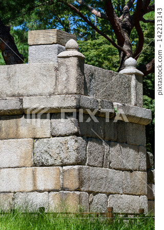 A weathered stone structure set against lush greenery, featuring intricate vertical walls 142213143