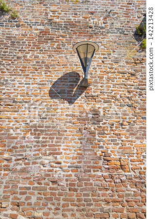 A modern lantern is mounted on a textured, weathered brick wall. A modern lantern is mounted on a textured, weathered brick wall. 142213428
