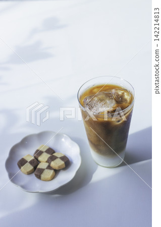 一杯冰拿鐵和幾塊餅乾沐浴在斑駁的陽光下,構成了一幅留白豐富的垂直夏日構圖。 一杯冰拿鐵和幾塊餅乾沐浴在斑駁的陽光下,構成了一幅留白豐富的垂直夏日構圖。 142214813