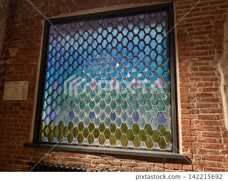 Stained glass window with hexagonal pattern set against red brick wall in warm interior lighting Stained glass window with hexagonal pattern set against red brick wall in warm interior lighting 142215692