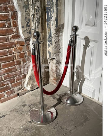 Red velvet rope barrier in an event entrance area with a rustic brick wall and a white door Red velvet rope barrier in an event entrance area with a rustic brick wall and a white door 142215693