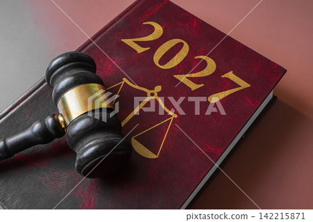 Judge wooden gavel on law book with scales of justice emblem and 2027 text Judge wooden gavel on law book with scales of justice emblem and 2027 text 142215871