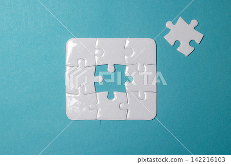 White jigsaw puzzle missing its center piece with the final piece placed nearby on a blue background. High Quality Photo White jigsaw puzzle missing its center piece with the final piece placed nearby on a blue background. High Quality Photo 142216103