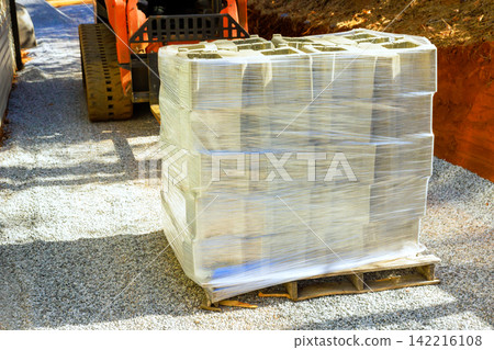 Workers get ready to use stacked concrete blocks at construction site with gravel machinery. Workers get ready to use stacked concrete blocks at construction site with gravel machinery. 142216108