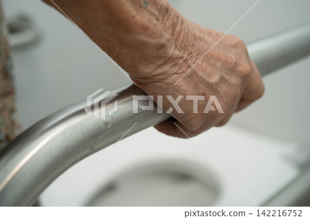 Asian elderly woman patient use toilet support rail in bathroom. Asian elderly woman patient use toilet support rail in bathroom. 142216752
