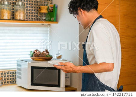 A man in an apron using a microwave in the kitchen. A man in an apron using a microwave in the kitchen. 142217731
