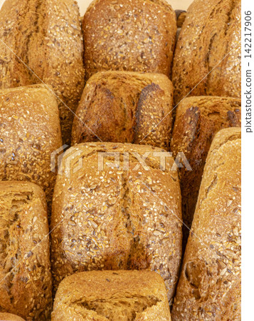 Whole grain artisan bread loaves close together with mixed seeds on top at a local bakery on a sunny day Whole grain artisan bread loaves close together with mixed seeds on top at a local bakery on a sunny day 142217906