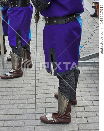 Participants in festival wearing bright purple tunics and metallic accessories walk on pavement in city square during celebration Participants in festival wearing bright purple tunics and metallic accessories walk on pavement in city square during celebration 142217913