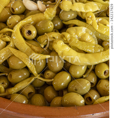 Glossy green olives with pickled yellow chili peppers in a clay bowl on a wooden table Glossy green olives with pickled yellow chili peppers in a clay bowl on a wooden table 142217929
