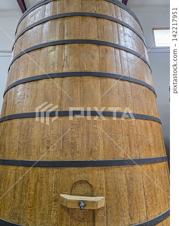 View from below of a large vintage wooden wine vat barrel with black iron hoops and a wooden tap spout in a wine cellar View from below of a large vintage wooden wine vat barrel with black iron hoops and a wooden tap spout in a wine cellar 142217951