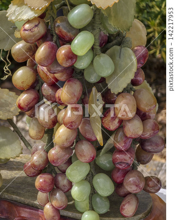 Close up shows ornate decorative sculpture of polished jade and gemstone grapes with carved leaves Close up shows ornate decorative sculpture of polished jade and gemstone grapes with carved leaves 142217953