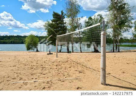 A beach volleyball court by a picturesque lake under a summer sky. A beach volleyball court by a picturesque lake under a summer sky. 142217975