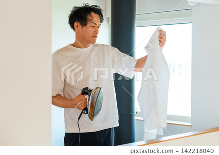 A middle-aged man ironing at home. A middle-aged man ironing at home. 142218040