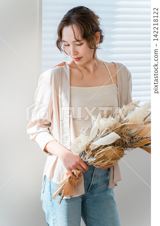 一位衣著時尚的女士手捧乾花，站在客廳窗邊。 142218122