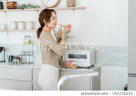 一位亞洲女性在廚房裡輕鬆地享用格蘭諾拉麥片早餐。 142218232