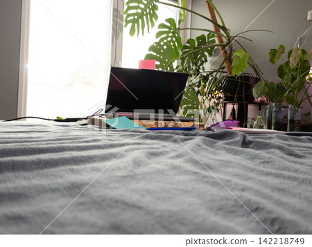 Laptop resting on a wooden block on a bed, screen off, with lush plants and natural light Laptop resting on a wooden block on a bed, screen off, with lush plants and natural light 142218749