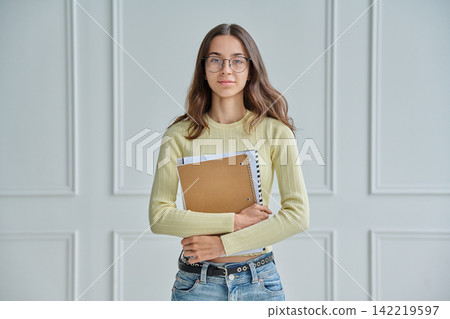 Portrait of young female college student holding notebooks against wall Portrait of young female college student holding notebooks against wall 142219597