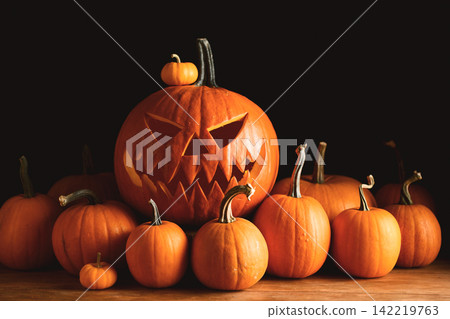 Carved pumpkin with scary face surrounded by an abundance of orange pumpkins Carved pumpkin with scary face surrounded by an abundance of orange pumpkins 142219763
