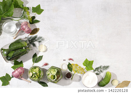 Cucumbers with dill, garlic, horseradish, pickling leaves, and pickled cucumbers in jars on the kitchen counter. Harvest concept. Recipe and ingredients for homemade pickles. Concept of home canning Cucumbers with dill, garlic, horseradish, pickling leaves, and pickled cucumbers in jars on the kitchen counter. Harvest concept. Recipe and ingredients for homemade pickles. Concept of home canning 142220128