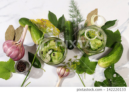 Cucumbers with dill, garlic, horseradish, pickling leaves, and pickled cucumbers in jars on the kitchen counter. Harvest concept. Recipe and ingredients for homemade pickles. Home canning Cucumbers with dill, garlic, horseradish, pickling leaves, and pickled cucumbers in jars on the kitchen counter. Harvest concept. Recipe and ingredients for homemade pickles. Home canning 142220133
