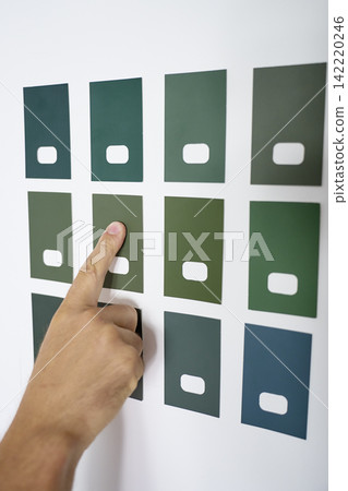 Hand points to one of several green paint color samples on white wall Hand points to one of several green paint color samples on white wall 142220246