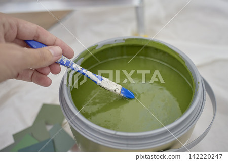 Hand mixes green paint with small brush in open paint can Hand mixes green paint with small brush in open paint can 142220247