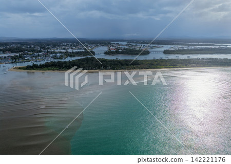 Aerial view of the Hastings River and surrounding islands in Port Macquarie, showcasing the striking contrast of brown floodwaters meeting clear turquoise water and creating distinct colour patterns 142221176