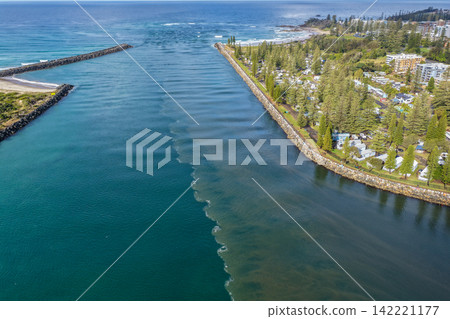 Aerial view looking through the Port Macquarie channel towards the Pacific Ocean, showing the caravan park, breakwalls and river entrance with a striking contrast between brown floodwaters Aerial view looking through the Port Macquarie channel towards the Pacific Ocean, showing the caravan park, breakwalls and river entrance with a striking contrast between brown floodwaters 142221177