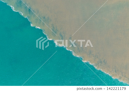 Aerial downward view of brown floodwaters flowing into the ocean and meeting clear turquoise seawater, creating a striking boundary of contrasting colours, sediment and swirling water patterns Aerial downward view of brown floodwaters flowing into the ocean and meeting clear turquoise seawater, creating a striking boundary of contrasting colours, sediment and swirling water patterns 142221179