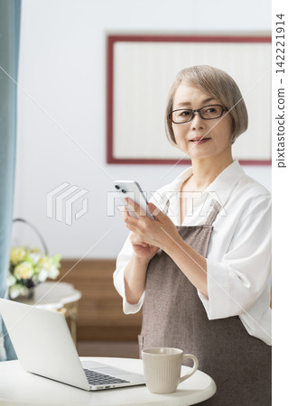 一位老婦人在客廳窗邊使用筆記型電腦。 一位老婦人在客廳窗邊使用筆記型電腦。 142221914
