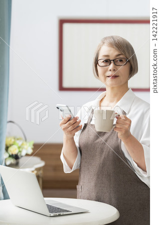 一位老婦人在客廳窗邊使用筆記型電腦。 142221917