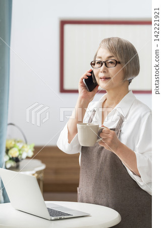 一位老婦人在客廳窗邊使用筆記型電腦。 一位老婦人在客廳窗邊使用筆記型電腦。 142221921