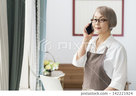 一位老婦人在客廳窗邊使用筆記型電腦。 142221924