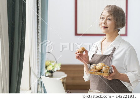 一位老婦人在客廳窗邊使用筆記型電腦。 一位老婦人在客廳窗邊使用筆記型電腦。 142221935