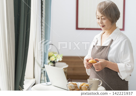 一位老婦人在客廳窗邊使用筆記型電腦。 一位老婦人在客廳窗邊使用筆記型電腦。 142221937