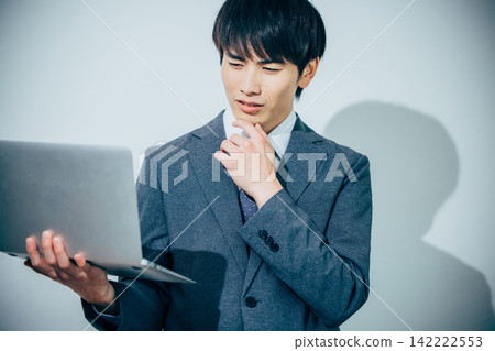 一個身穿西裝的男人，手裡拿著筆記型電腦，正在思考。 142222553