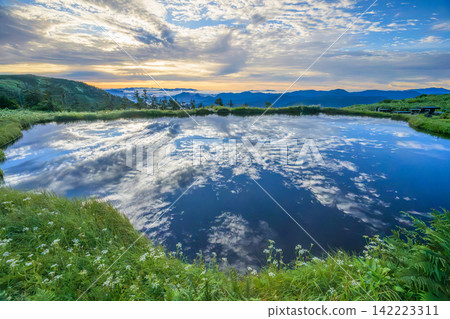 The sunrise over Komano-Oike Pond near the summit of Mt. Aizu-Komagatake and the reflection of the clouds on its surface. The sunrise over Komano-Oike Pond near the summit of Mt. Aizu-Komagatake and the reflection of the clouds on its surface. 142223311