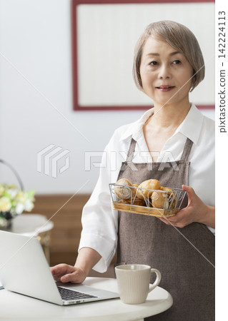 一位老婦人在客廳窗邊使用筆記型電腦。 一位老婦人在客廳窗邊使用筆記型電腦。 142224113