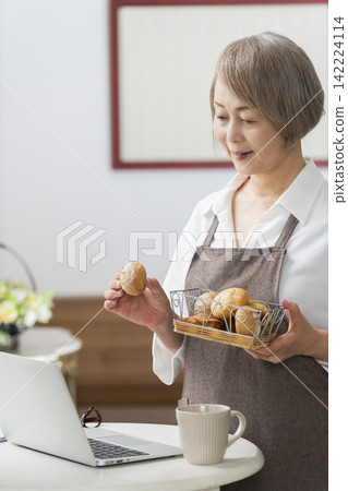 一位老婦人在客廳窗邊使用筆記型電腦。 一位老婦人在客廳窗邊使用筆記型電腦。 142224114